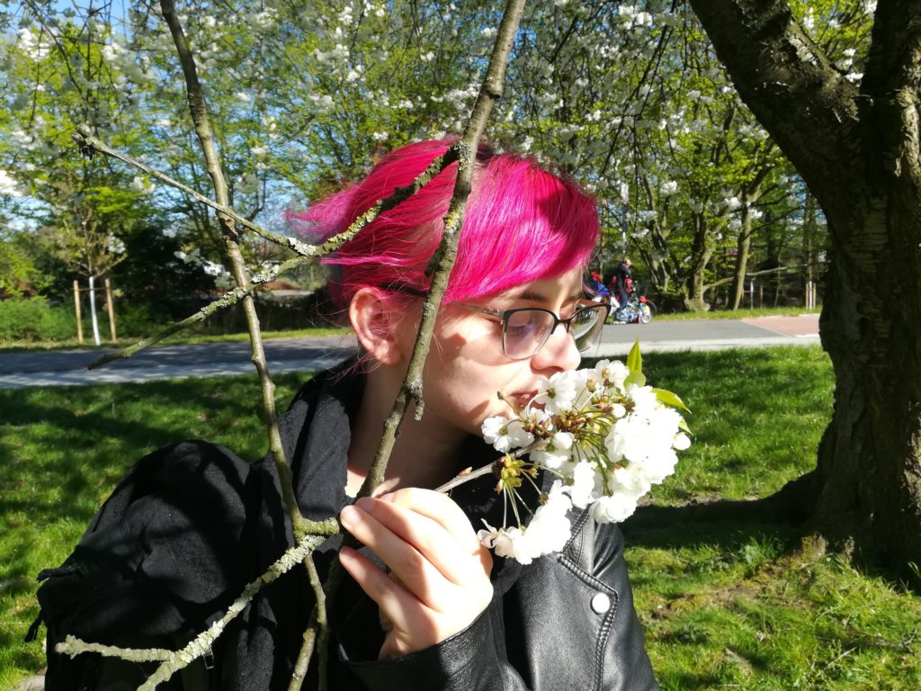 Lucia steht im Grünen und riecht an der weißen Blüte eines Baumes.